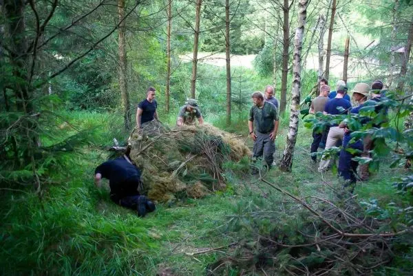Gruppe arbeitet an einer improvisierten Unterkunft aus Ästen und Gras im Wald