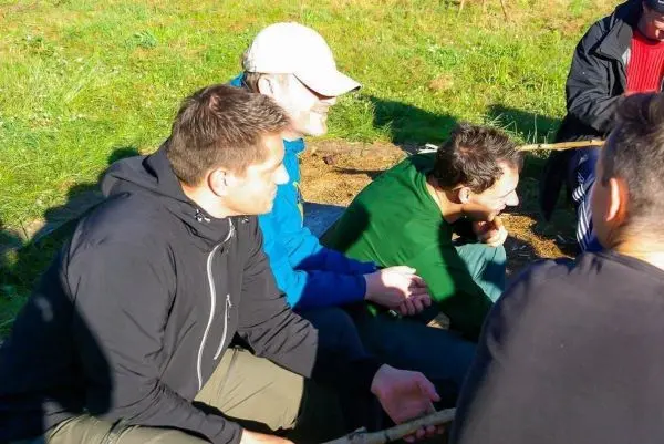Gruppe sitzt im Gras und hält Stöcke in der Hand