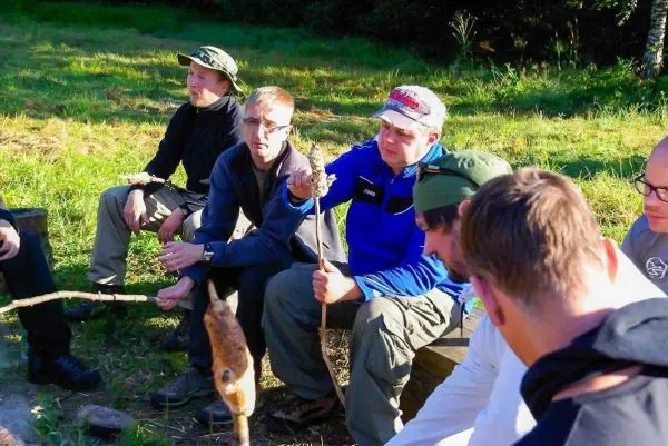 Gruppe sitzt im Kreis und röstet Lebensmittel über einem offenen Feuer