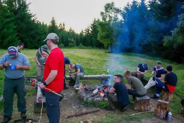 Gruppe sitzt um ein Feuer und bereitet Essen vor beim Survival Training
