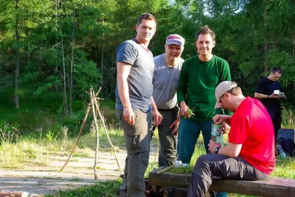 Gruppe von vier Personen steht um einen Tisch im Freien, Holzgestell im Hintergrund
