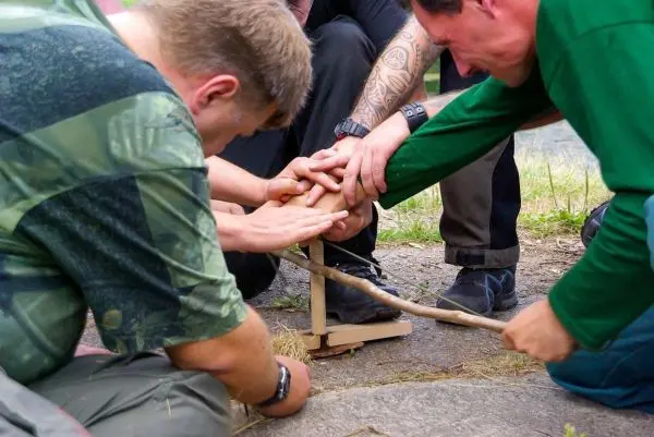 Gruppierung arbeitet gemeinsam an einem Feuerbohrer zur Zundererzeugung