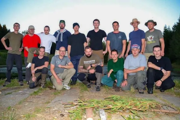 Gruppierung von Männern in Outdoor-Bekleidung auf einem Steinboden, umgeben von Bäumen