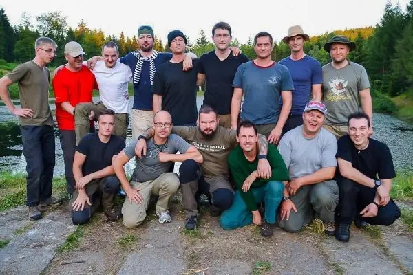 Gruppierung von Personen auf einem Weg neben einem Gewässer, umgeben von Bäumen