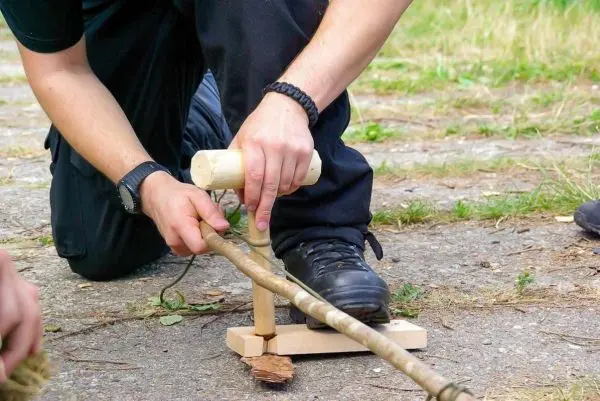 Holzstück wird mit einem Holzhammer auf einer selbstgebauten Feuerbohrvorrichtung bearbeitet