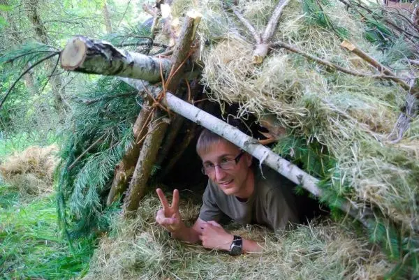 Improvisierte Tarp-Notunterkunft aus Ästen und Gras, Person schaut heraus