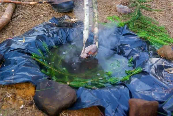 Kessel mit Wasser dampft über Feuerstelle aus Steinen und Ästen