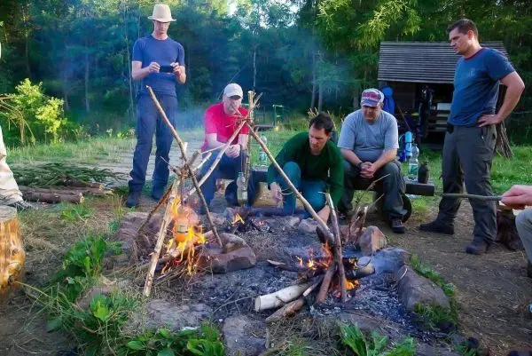 Kleine Flamme brennt in einem Steinkreis, mehrere Personen stehen um das Feuer