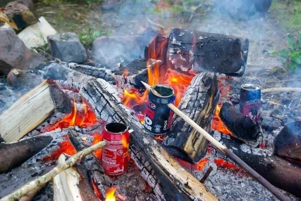 Kleine Flamme brennt zwischen Holzscheiten und Dosen