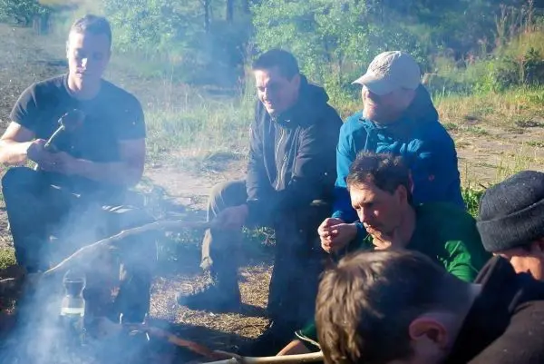 Lagerfeuer mit mehreren Personen, die um das Feuer sitzen und sich unterhalten