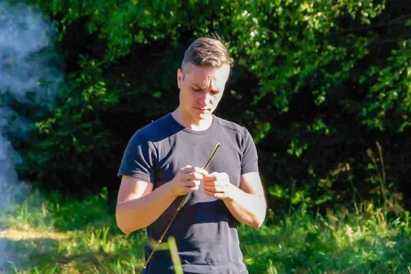 Mann bearbeitet einen Stock im Freien, Rauch steigt im Hintergrund auf