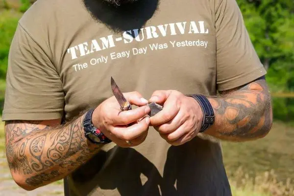 Mann hält ein Messer und bearbeitet einen Stein am Ufer eines Gewässers