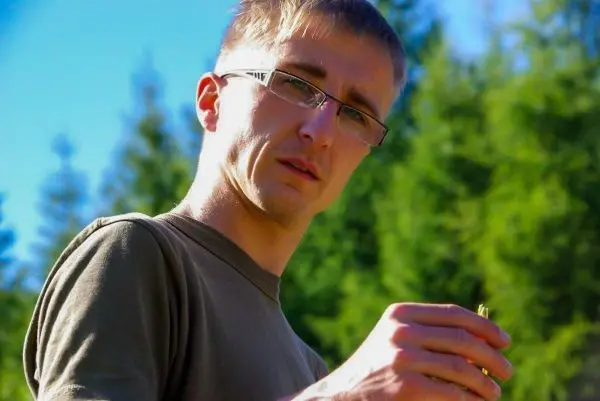 Mann hält einen kleinen Gegenstand in der Hand, Blick auf die Kamera gerichtet