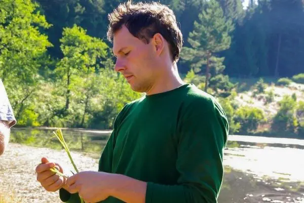 Mann hält grüne Pflanzenstängel am Ufer eines Gewässers