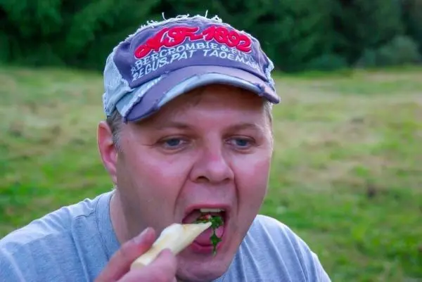 Mann isst mit einem Holzstück Kräuter im Freien