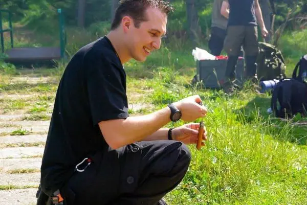 Mann kniet im Gras und hält ein Messer in der Hand