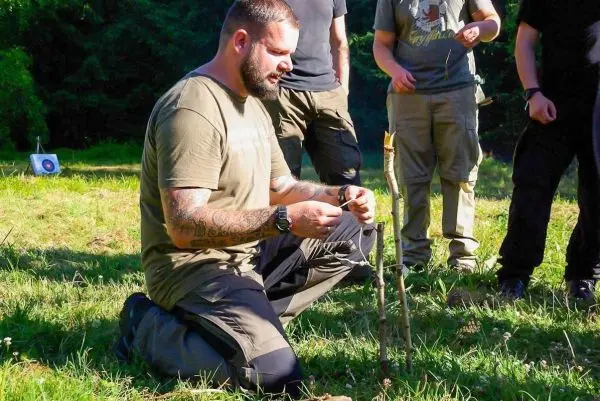 Mann kniet und bindet eine Schnur um einen Stock zur Konstruktion einer Falle