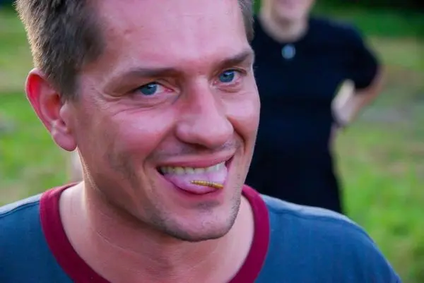 Mann mit Holzstück auf der Zunge lächelt in die Kamera