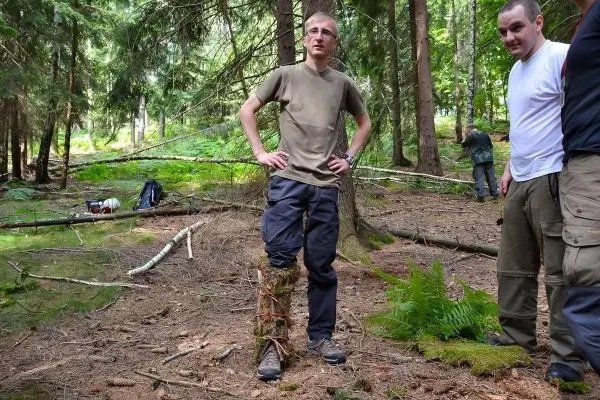 Mann mit improvisierter Beinprothese aus Ästen steht im Wald