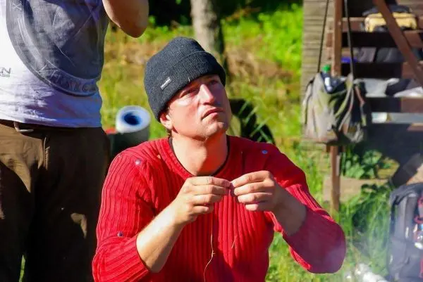 Mann mit rotem Pullover fädelt einen Faden durch eine Nadel