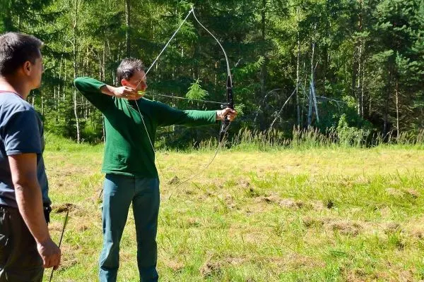 Mann spannt einen Bogen im Freien, während ein anderer zuschaut