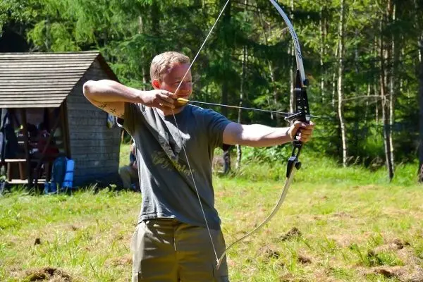 Mann spannt einen Bogen und zielt auf ein Ziel im Freien
