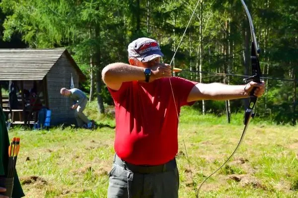 Mann spannt einen Bogen und zielt auf ein Ziel im Wald