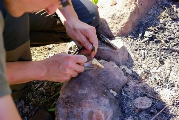 Messer schnitzt Zunder auf einem großen Stein neben einem Feuerplatz