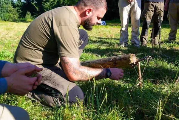 Person bearbeitet einen Holzstock auf dem Boden beim Überlebenstraining