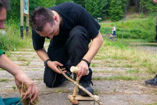 Person bearbeitet einen Stock mit einem Werkzeug beim Überlebenstraining
