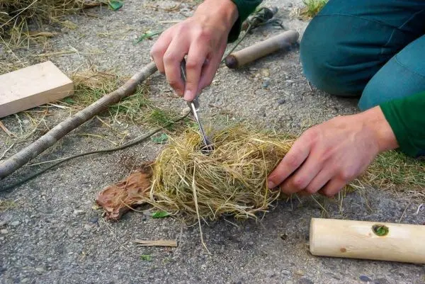 Person bereitet Zunder aus Gras und Holzstücken vor beim Survival Training