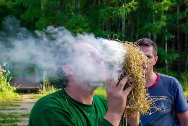 Person bläst Rauch aus einer Handvoll trockenem Gras
