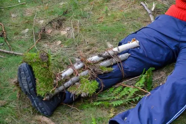 Person fixiert Äste an Bein mit Schnur im Wald