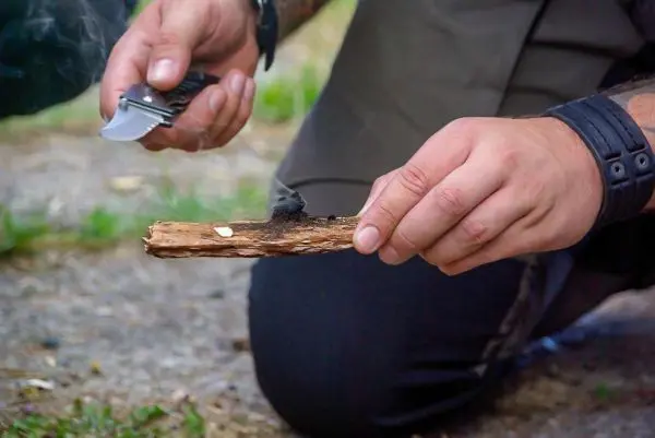 Person hält ein Stück Holz und schneidet mit einem Messer daran