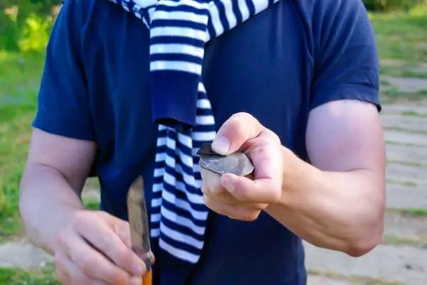 Person hält einen Stein und ein Werkzeug in der Hand