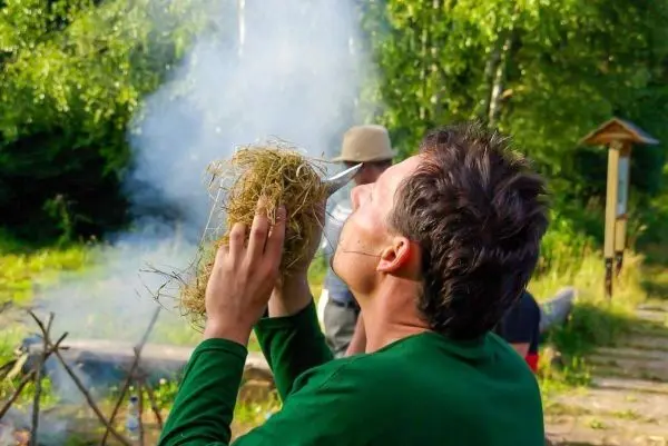 Person hält trockenes Gras in der Hand und pustet darauf