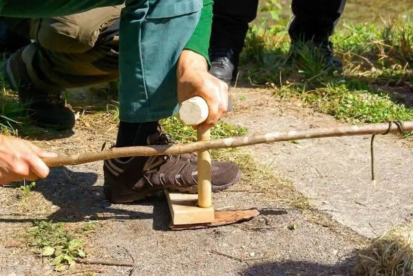 Person nutzt einen Feuerbohrer auf dem Boden beim Überlebenstraining