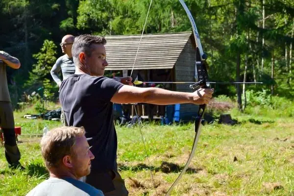 Person zielt mit einem Bogen auf ein Ziel beim Outdoorkurs
