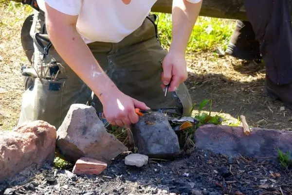 Person zündet Feuer mit einem Feuerstein und einem Zündholz