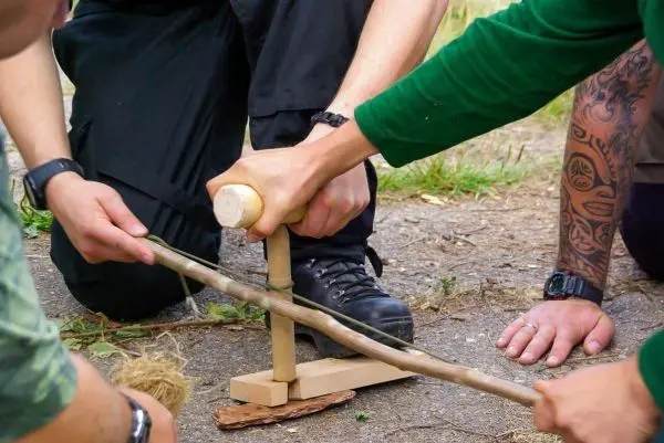 Personen bauen eine Feuerstelle mit Holz und Schnur beim Überlebenstraining