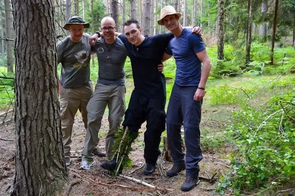 Vier Personen stehen lächelnd im Wald und posieren für ein Foto