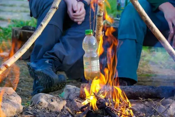 Wasserflasche hängt über einem Feuer auf einer improvisierten Halterung