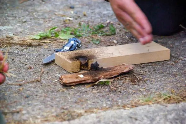 Zunder glimmt auf Holzstück, während Hand eine Bewegung macht
