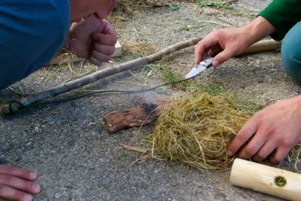 Zunder glimmt auf Holzstück, während Messer und Hände aktiv sind