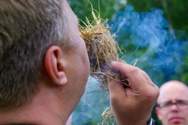 Zunder glimmt in der Hand, Rauch steigt auf