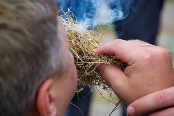 Zunder glimmt und Rauch steigt auf, während Zunder gehalten wird