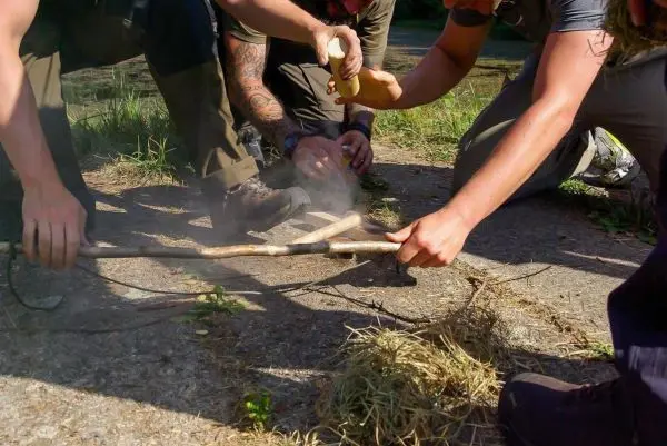 Zunder glimmt, während zwei Holzstücke zur Feuererzeugung bearbeitet werden