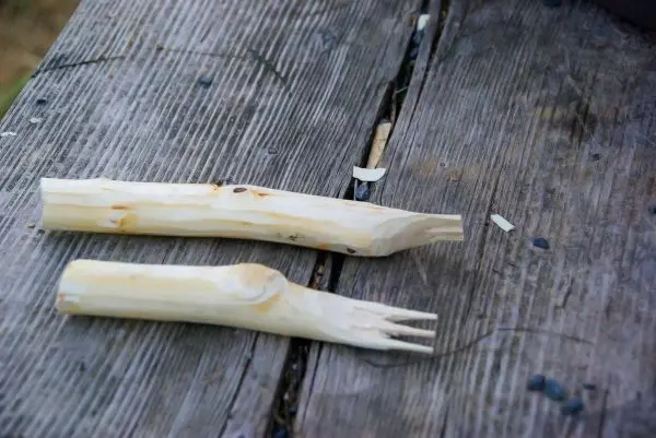 Zwei geschnitzte Holzstücke liegen auf einer Holzoberfläche, eines mit Gabelzinken