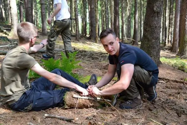 Zwei Personen arbeiten am Boden mit Holzstücken in einem Waldgebiet