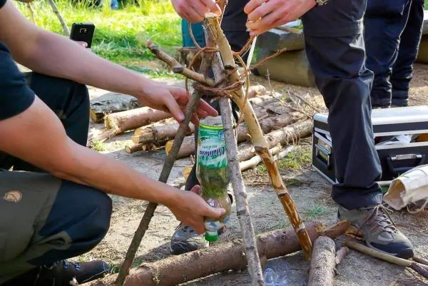 Zwei Personen bauen eine improvisierte Halterung aus Ästen für eine Wasserflasche